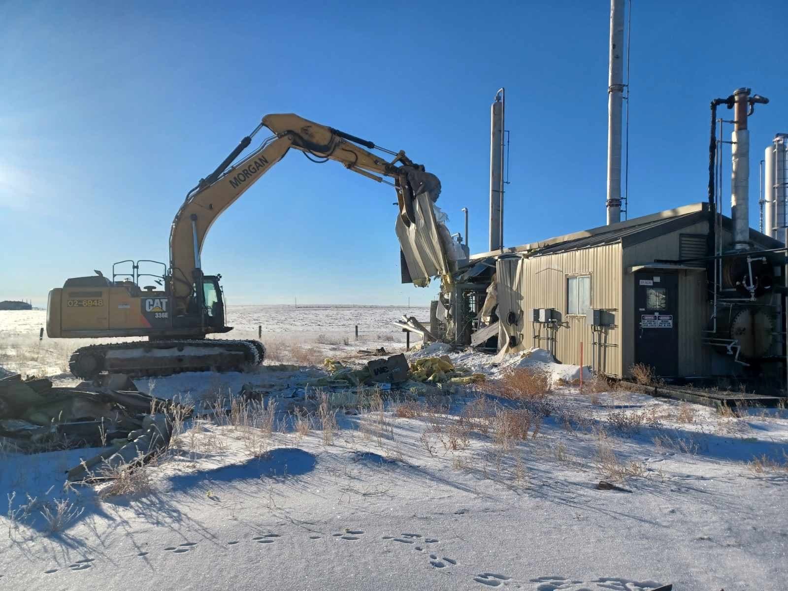 Yellow construction machinery tearing apart a building underneath a blue sky in the winter.