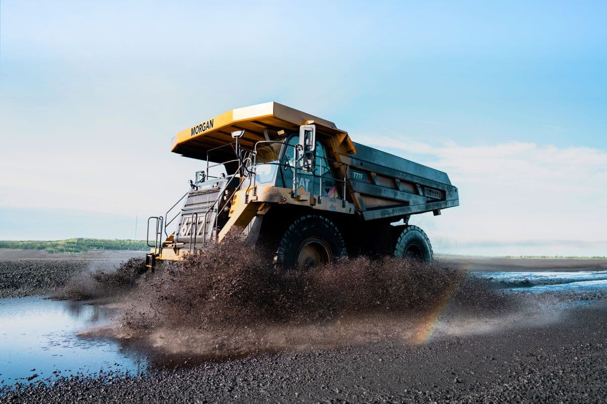A yellow dump truck driving through water on a dirt road.